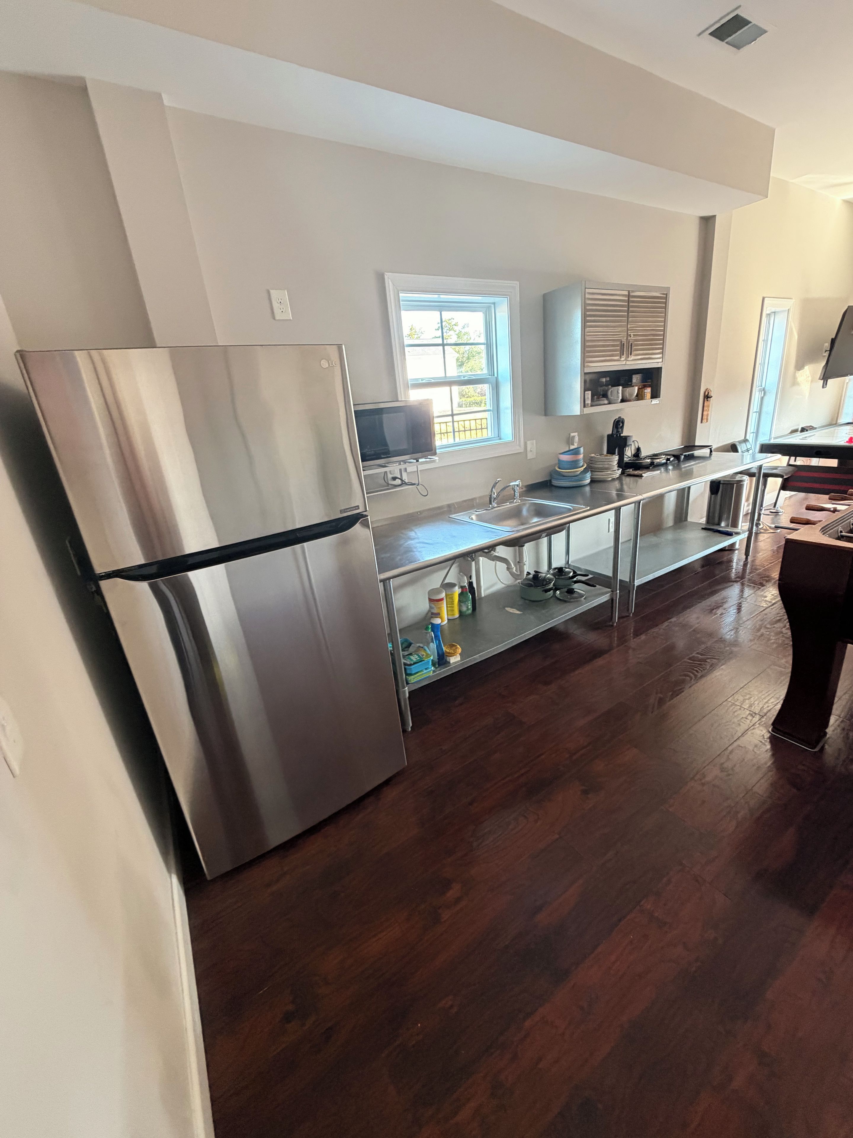 A modern kitchen with stainless steel appliances, a window, and wooden flooring.