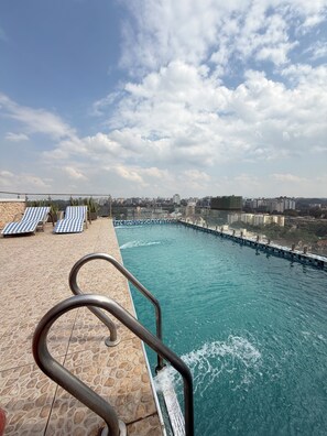 Una piscina en la azotea con agua azul cristalina, sillas de descanso y vistas a la ciudad.