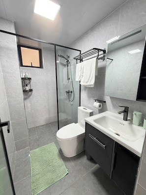 Un baño moderno con ducha envuelta en vidrio, inodoro, lavamanos y espejo.