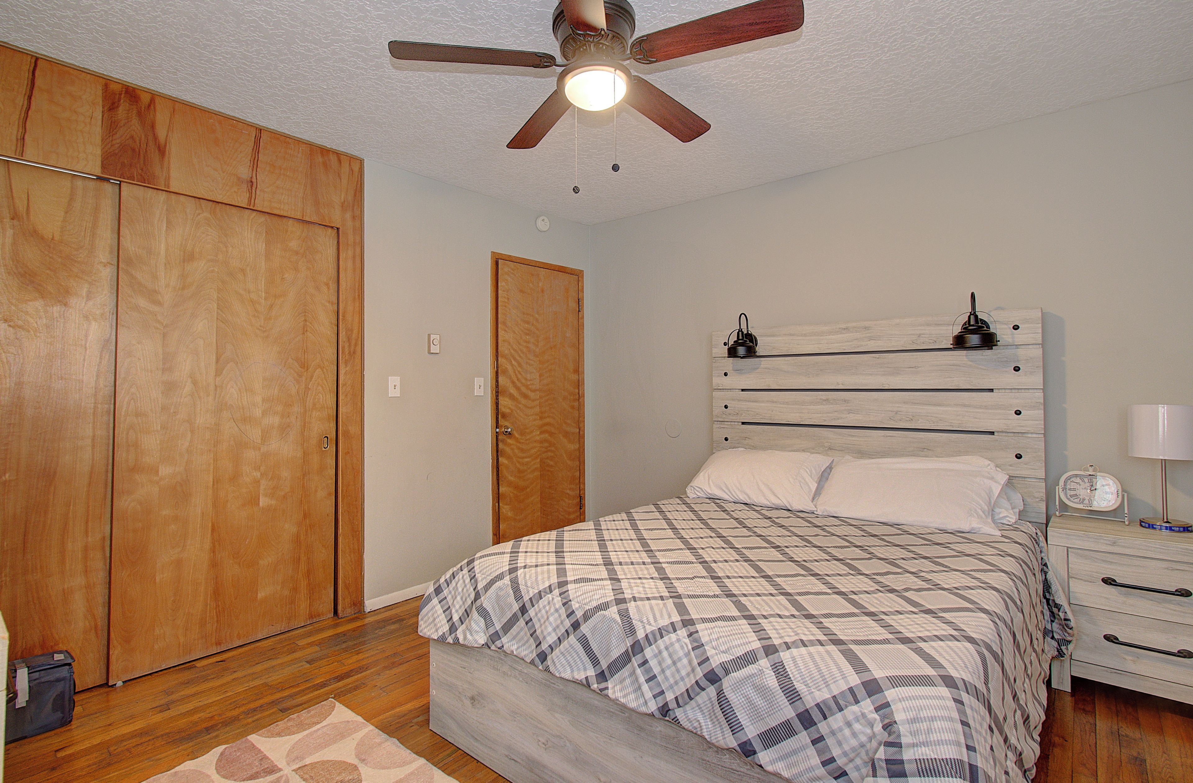 A bedroom with a bed, a nightstand, a clock, a ceiling fan, and wooden wardrobes.