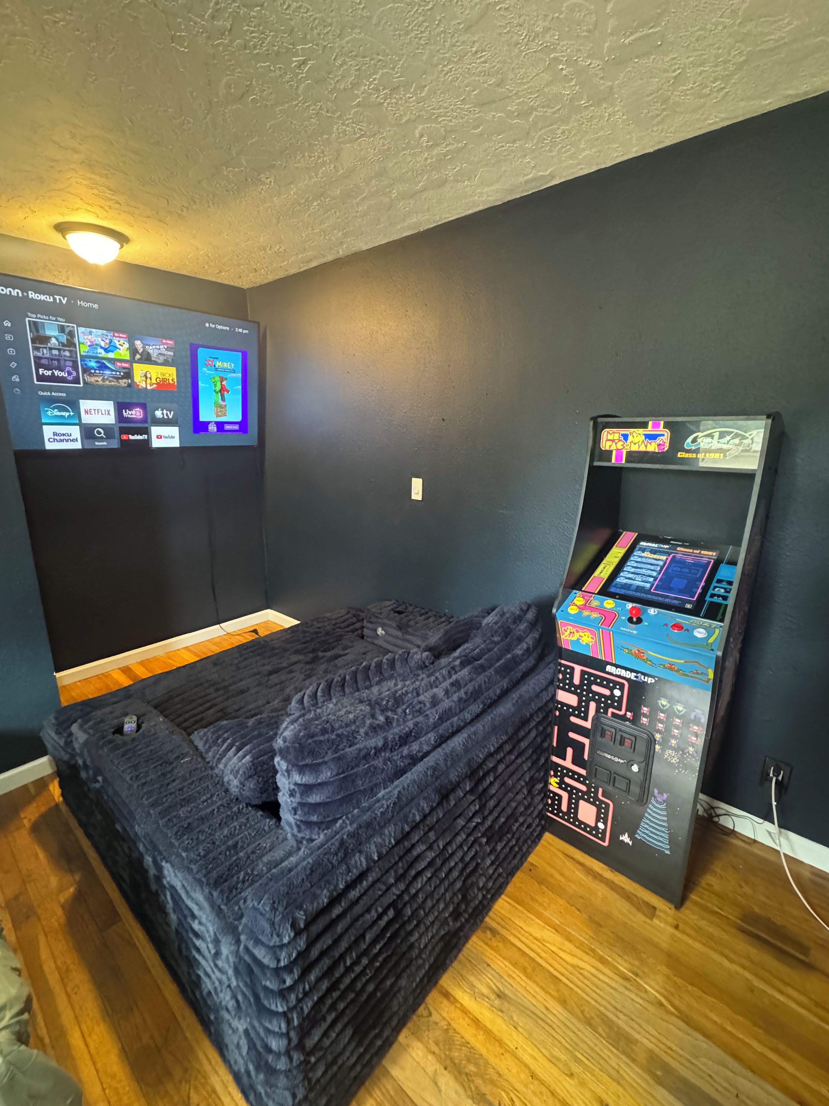 A room with a bed, a wall-mounted TV, and a gaming console.