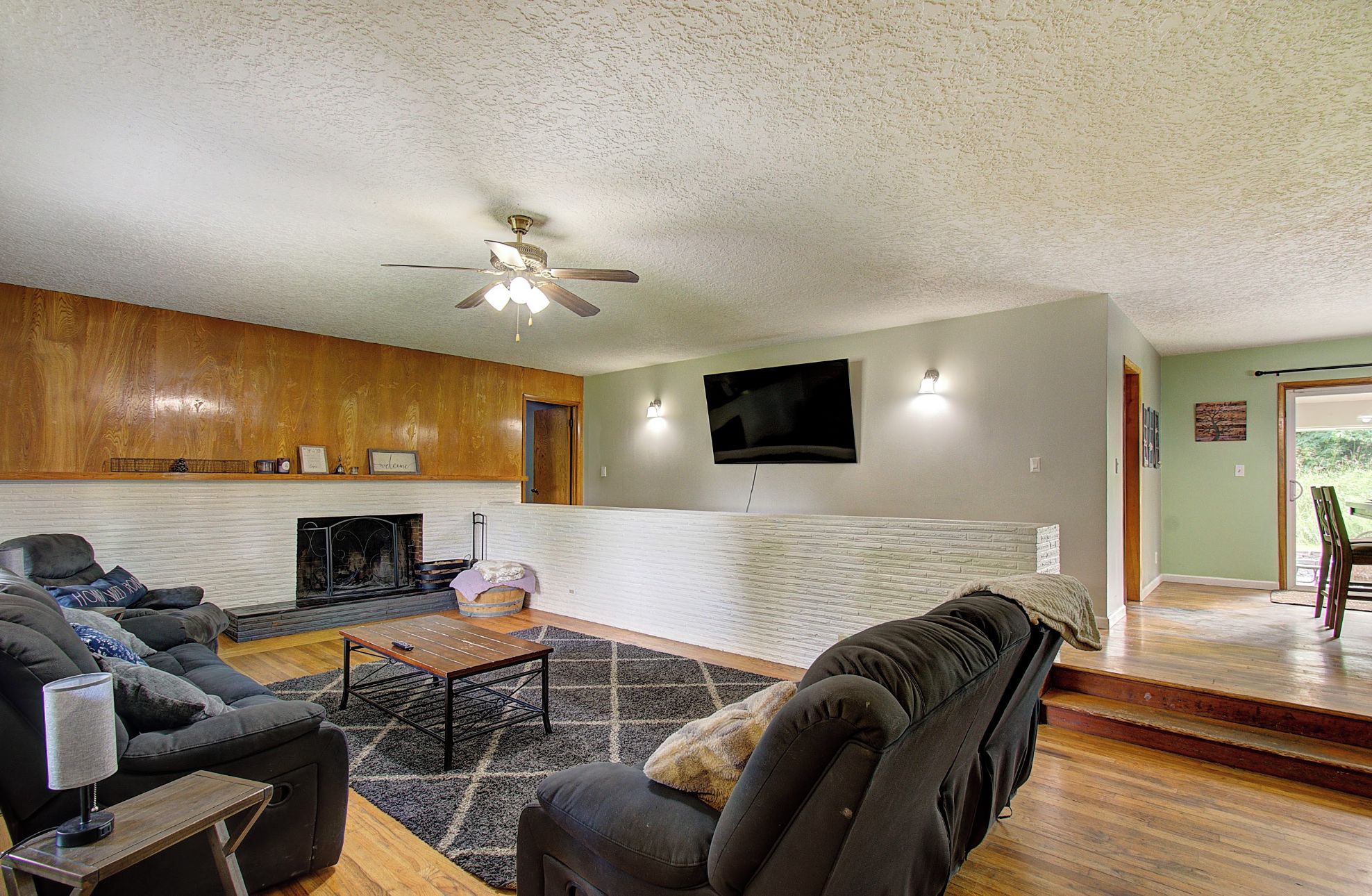 A living room with a fireplace, a ceiling fan, a flat-screen TV, and a staircase leading to another room.