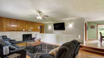 A living room with a fireplace, a ceiling fan, a flat-screen TV, and a staircase leading to another room.