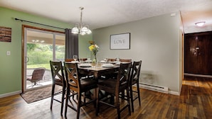 Une salle à manger avec une table dressée pour six personnes, un lustre et une citation encadrée accrochée au mur.