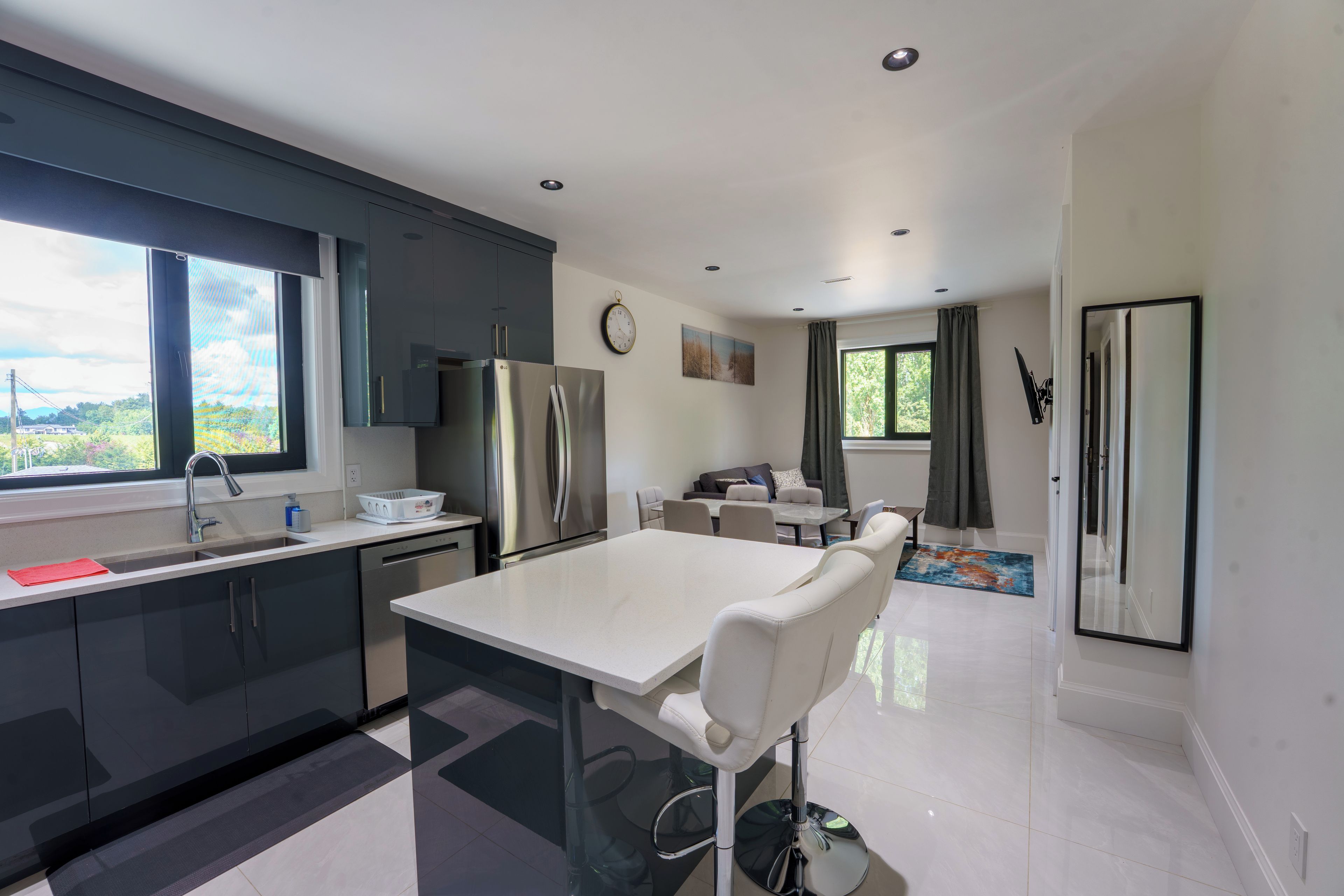 A modern kitchen with a central island, a dining area with a table and chairs, and a view of greenery outside.