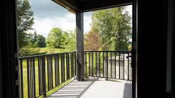 Een overdekt terras met een zwarte metalen balustrade, een betonnen vloer en uitzicht op een grasveld en bomen.