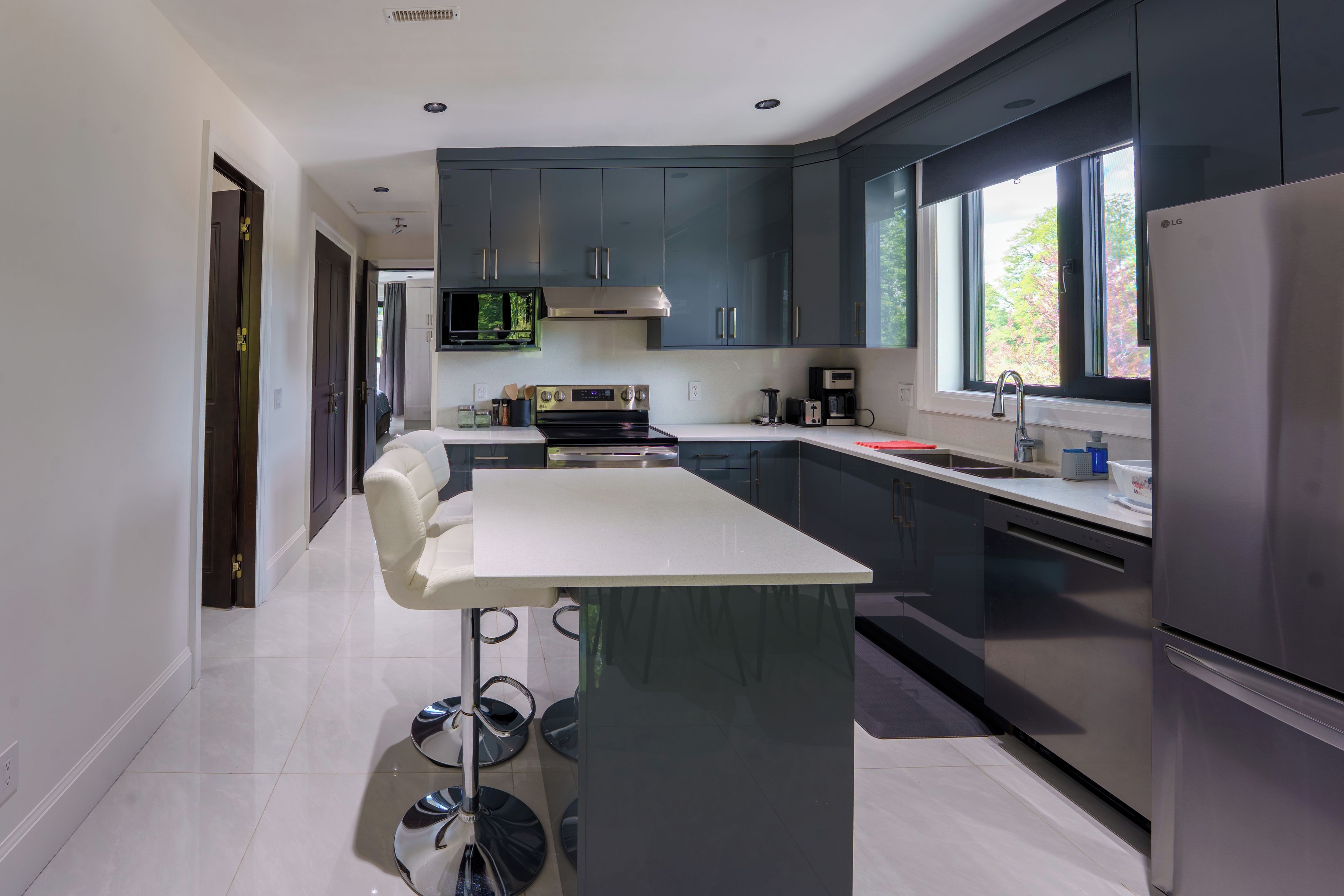 A modern kitchen with dark cabinets, a central island, stainless steel appliances, and a window providing natural light.
