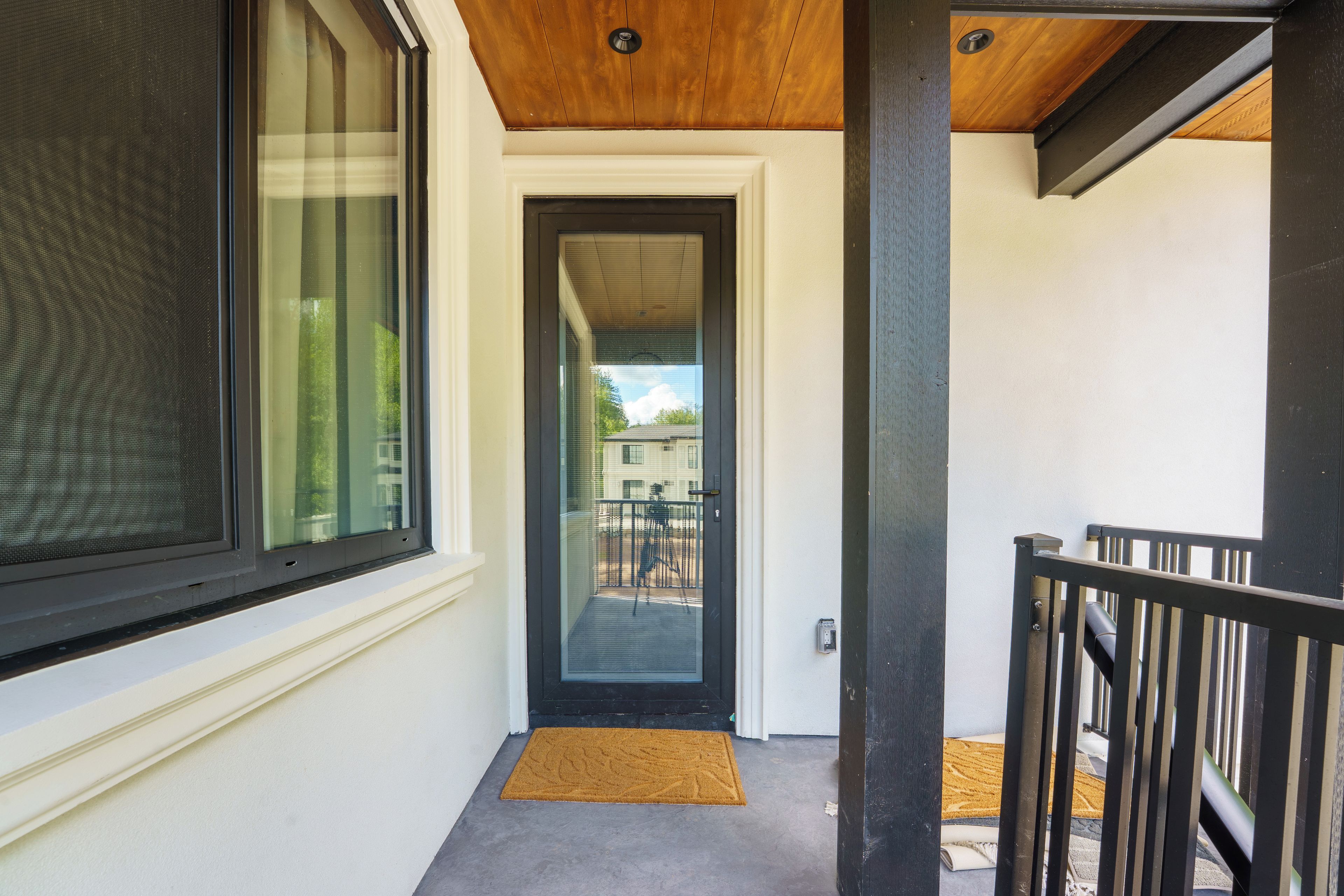 A modern building entrance with a glass door, a black metal railing, and a doormat.