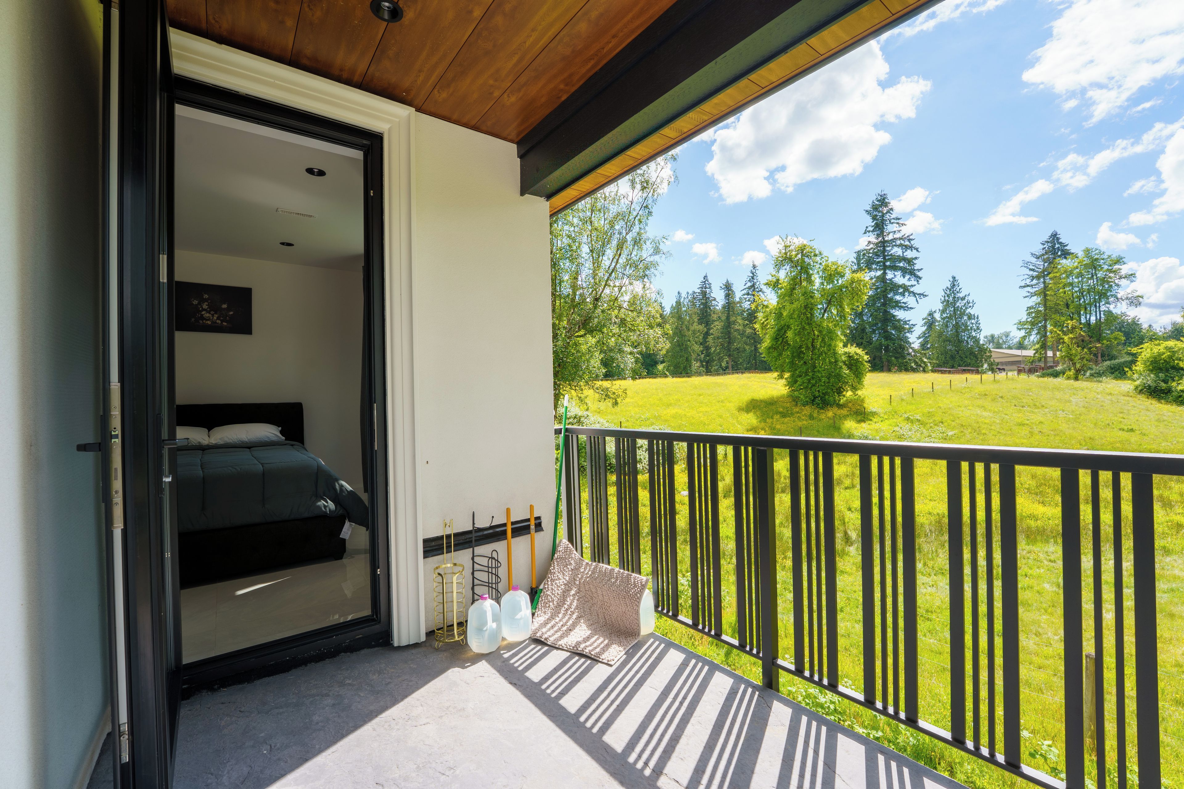 A balcony with a bed, a view of a green field, and a wooden ceiling.