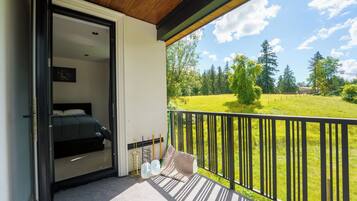 A balcony with a bed, a view of a green field, and a wooden ceiling.