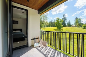 Ein Balkon mit einem Bett, Blick auf ein grünes Feld und einer Holzbalkendecke.