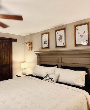 Un dormitorio con una cama, una mesita de noche, una lámpara y tres cuadros en la pared.