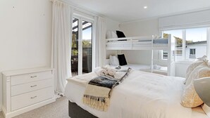 Un dormitorio con una cama litera, una mesita de noche, una cómoda y vistas a través de una puerta corrediza.