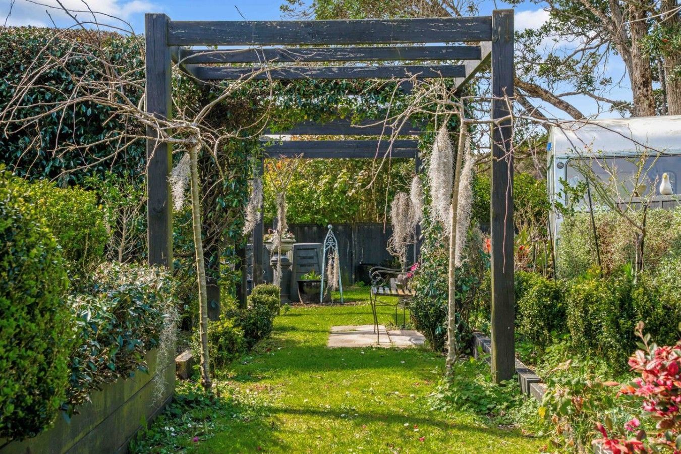 A garden with a wooden pergola, a pathway, and various plants.