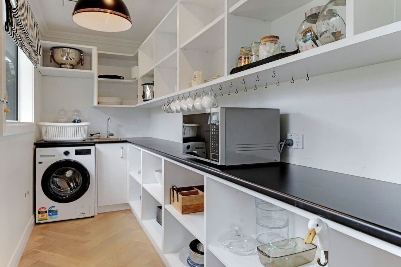 A modern kitchen with a built-in washing machine, a microwave, and a variety of storage shelves.