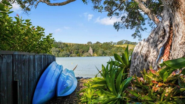 Una cerca de madera, un kayak azul y plantas tropicales junto a un lago.