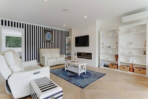 Un salon moderne avec un canapé blanc, un pouf à rayures, une table basse et une cheminée.