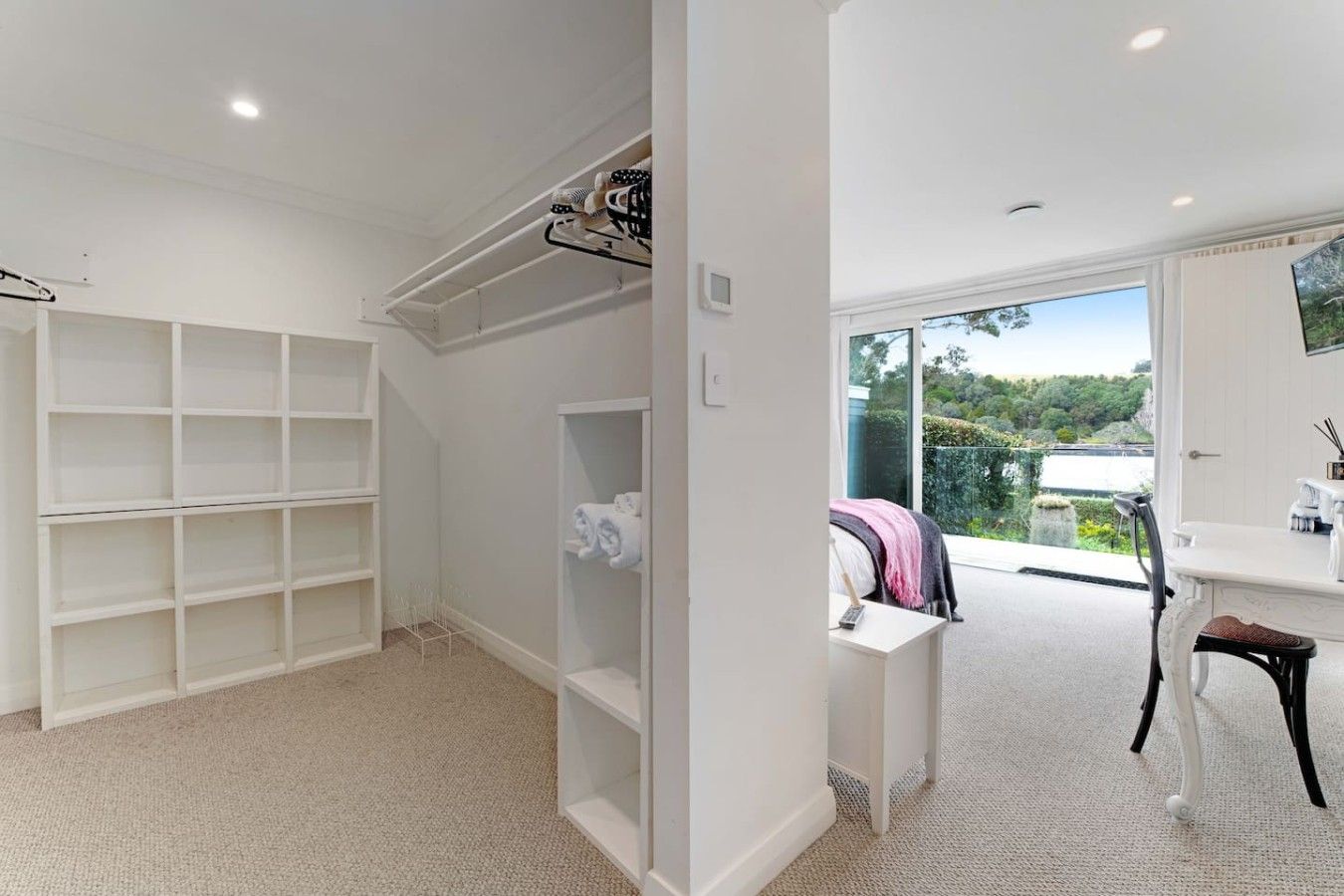 A modern bedroom with a large window, a built-in wardrobe, and a seating area with a view of the outdoors.