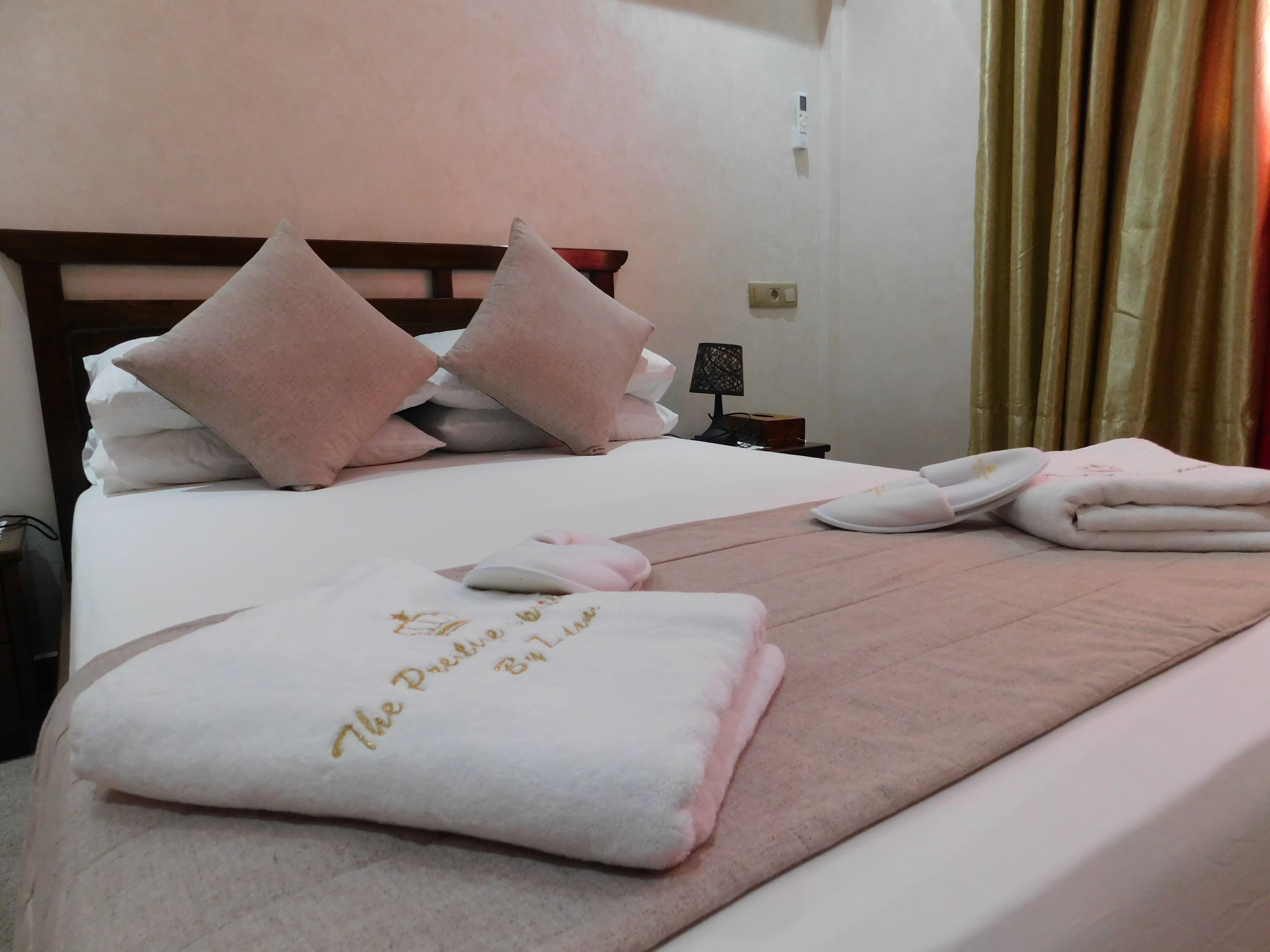 A neatly made bed with pink and white pillows, a folded towel with text, and a bedside lamp.