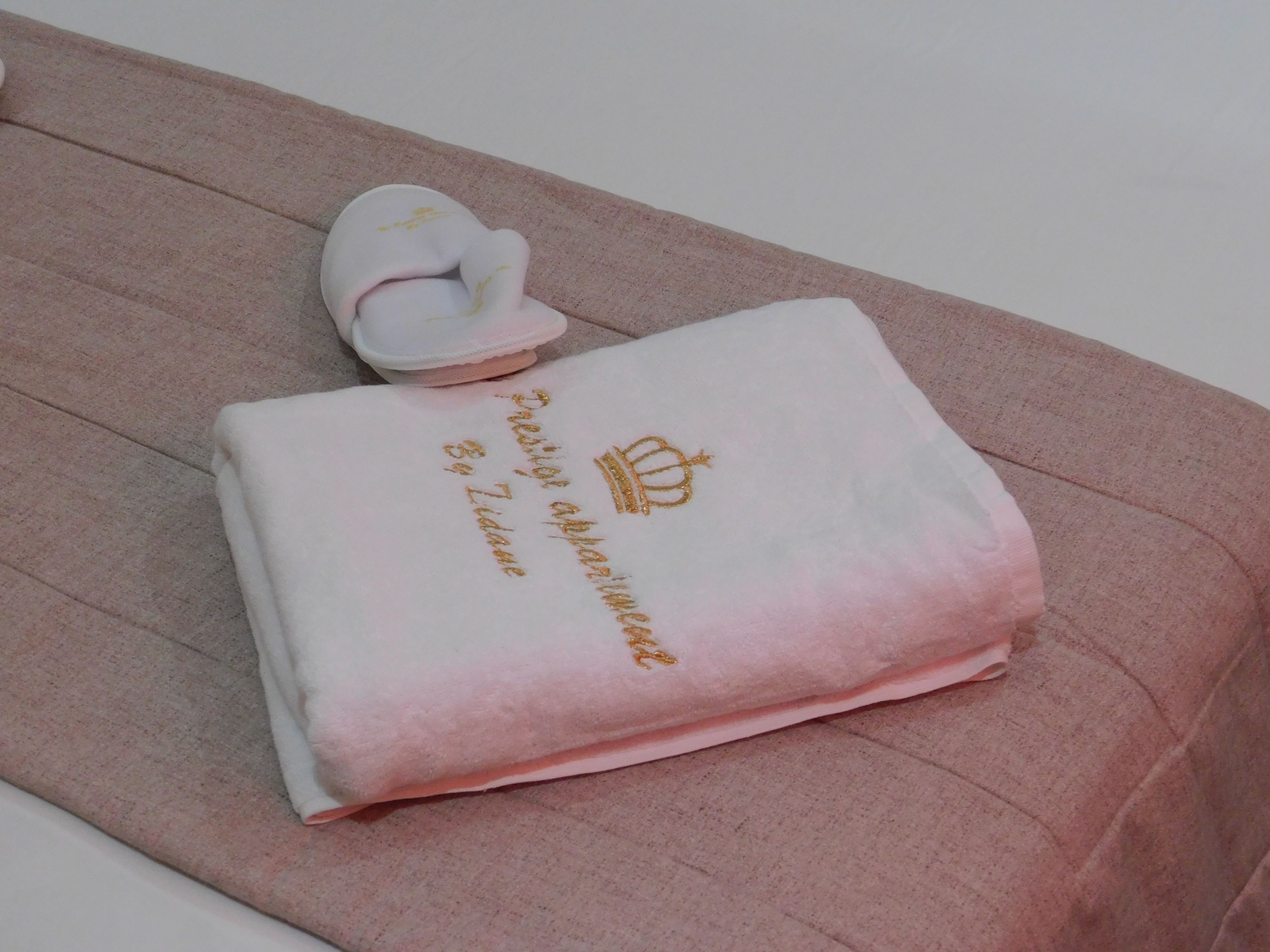 En prydligt vikt handduk med broderad text och en kronsymbol, placerad på en rosa, strukturerad yta.