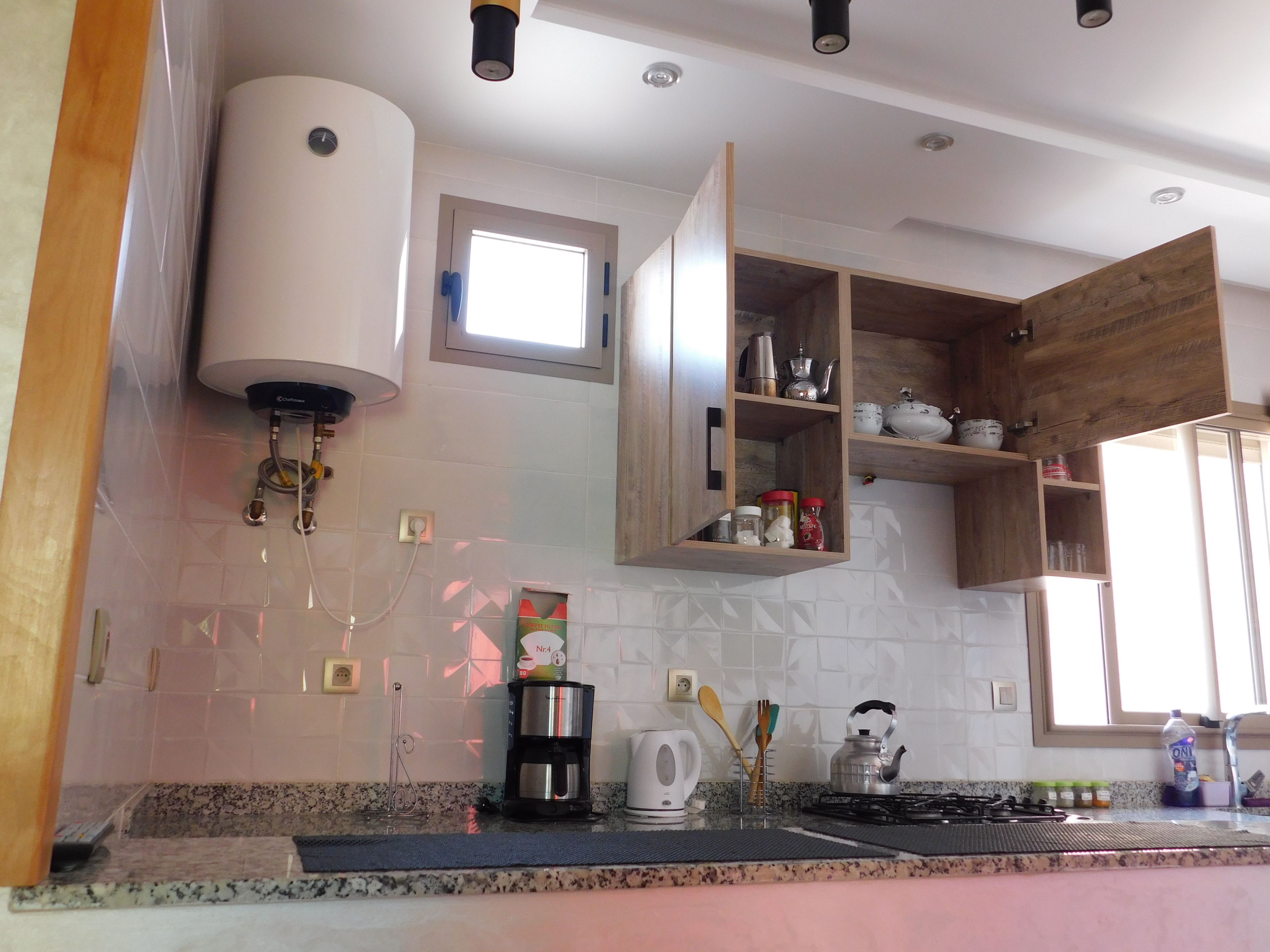 Una cocina con estufa a gas, cafetera, hervidor y armarios de madera.