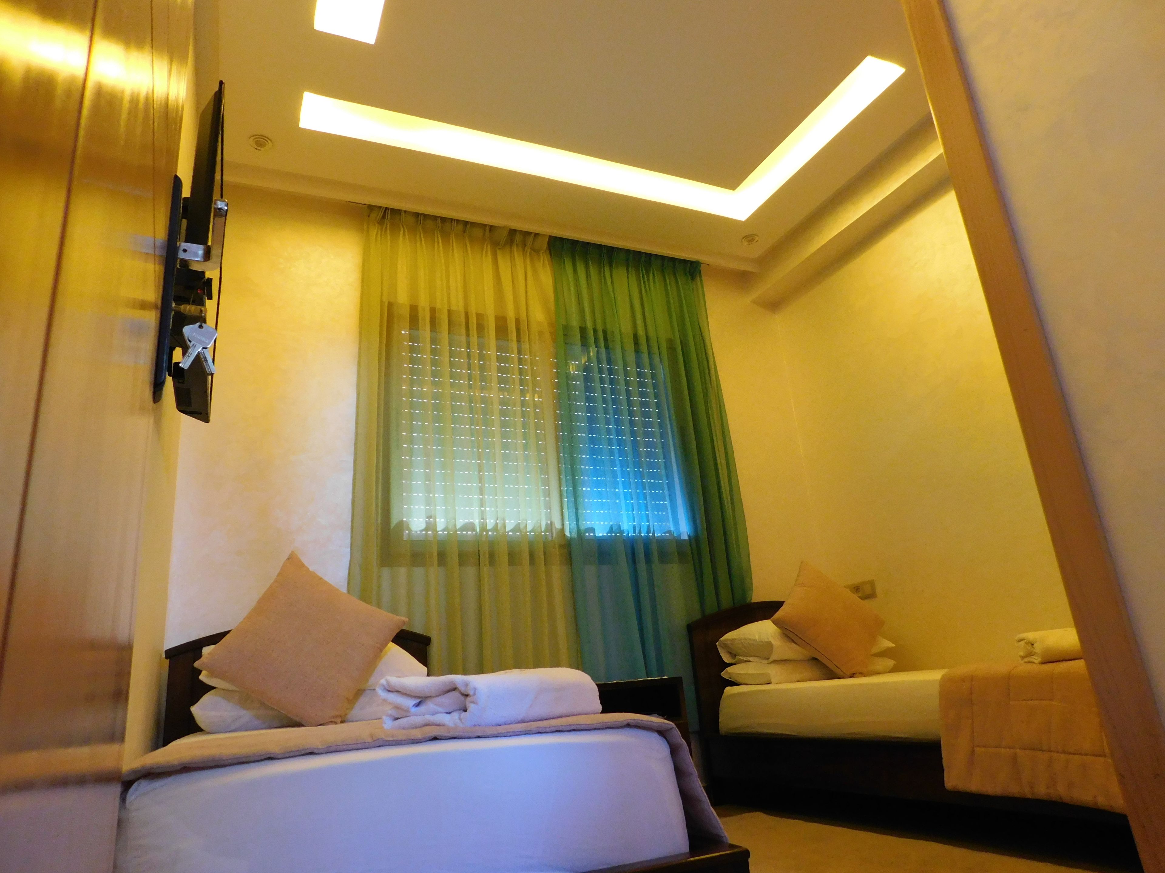 A hotel room with a bed, a bedside table, a window with curtains, and a wall-mounted TV.
