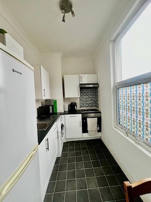 A compact kitchen with a refrigerator, stove, and washing machine. - Apartment Sleeps 4 Near Station (London)