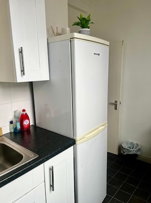A kitchen with a white refrigerator, a sink, and a potted plant on top of the fridge. - Apartment Sleeps 4 Near Station (London)