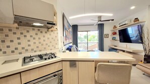 Une cuisine moderne équipée d’une cuisinière à gaz intégrée, d’un four et d’un four à micro-ondes. On y trouve un grand îlot central avec un tabouret, ainsi qu’un téléviseur à écran plat fixé au mur.
