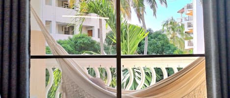 A room with a view of a building, a hammock, and a balcony railing.