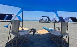 Uma praia com duas tendas e duas cadeiras dobráveis sob um toldo azul.