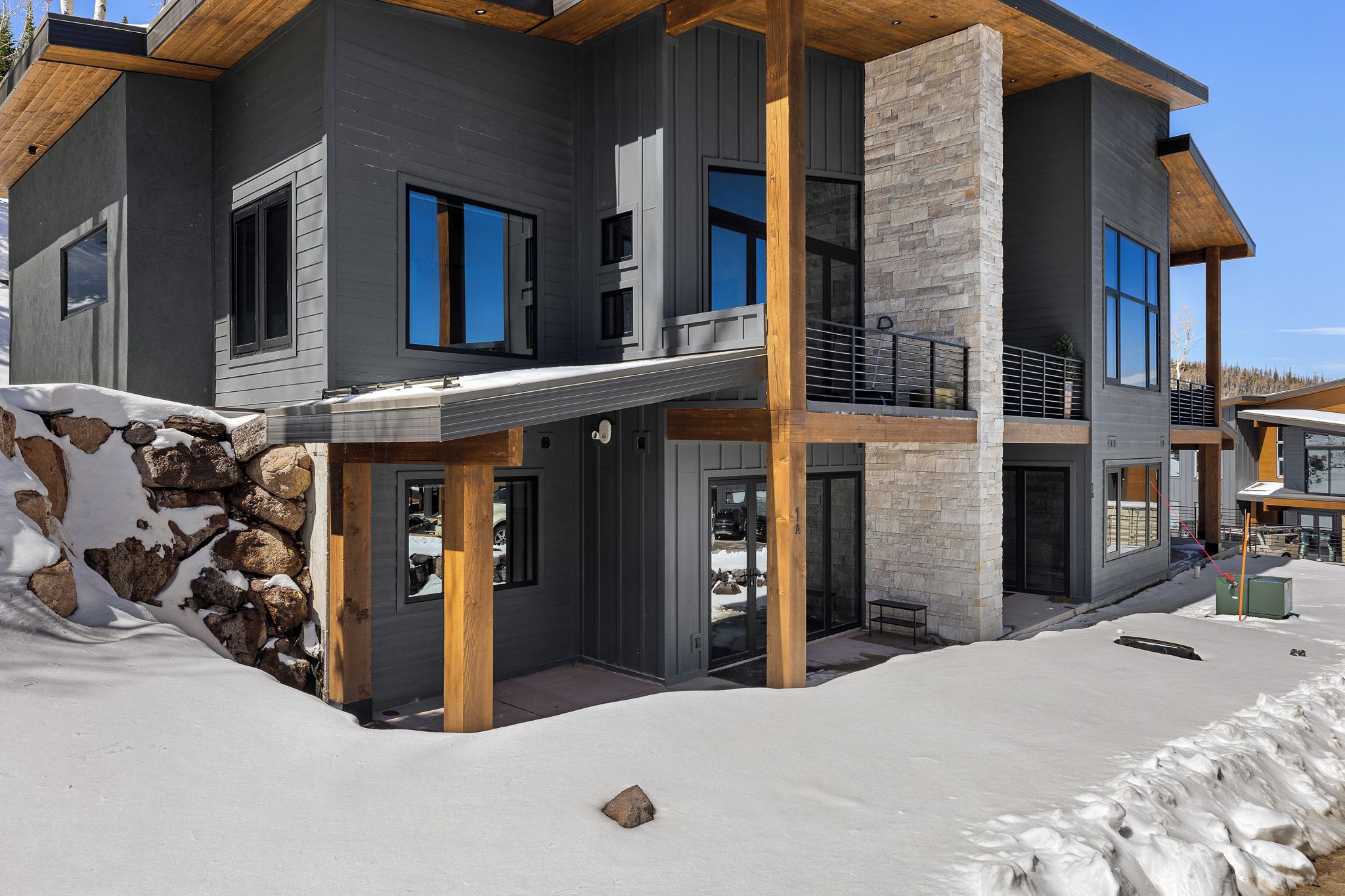 A modern two-story house with a stone facade, large windows, and a wooden deck.