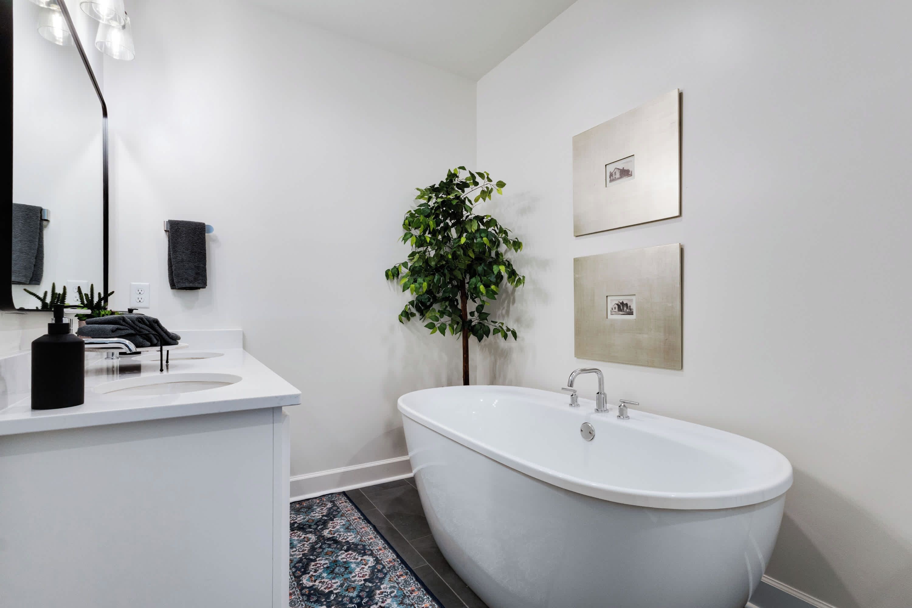 Ein modernes Badezimmer mit einer freistehenden Badewanne, einem weißen Waschtisch mit Spiegel und einer Topfpflanze.