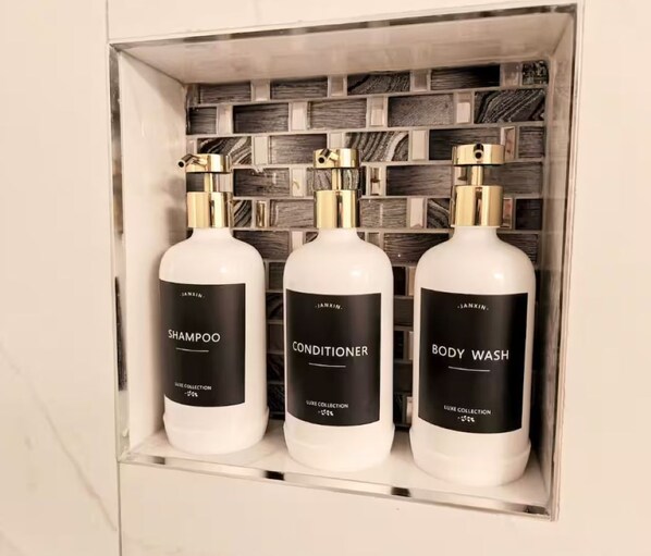 Prateleira no banheiro com três frascos de shampoo, condicionador e sabonete líquido.