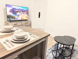 A modern kitchen with a wooden countertop, a television displaying a scenic view, and a dining area with a black marble table and two chairs. - Modern 2BR Luxury suite | White Rock (Surrey)