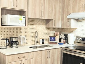 A modern kitchen with wooden cabinets, a microwave, a coffee maker, a sink, and a stove. - Modern 2BR Luxury suite | White Rock (Surrey)