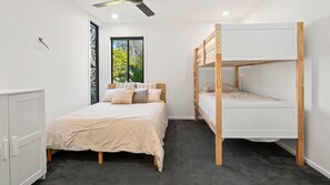 Une chambre avec un lit superposé, un lit simple, une armoire et une fenêtre donnant sur un paysage verdoyant.