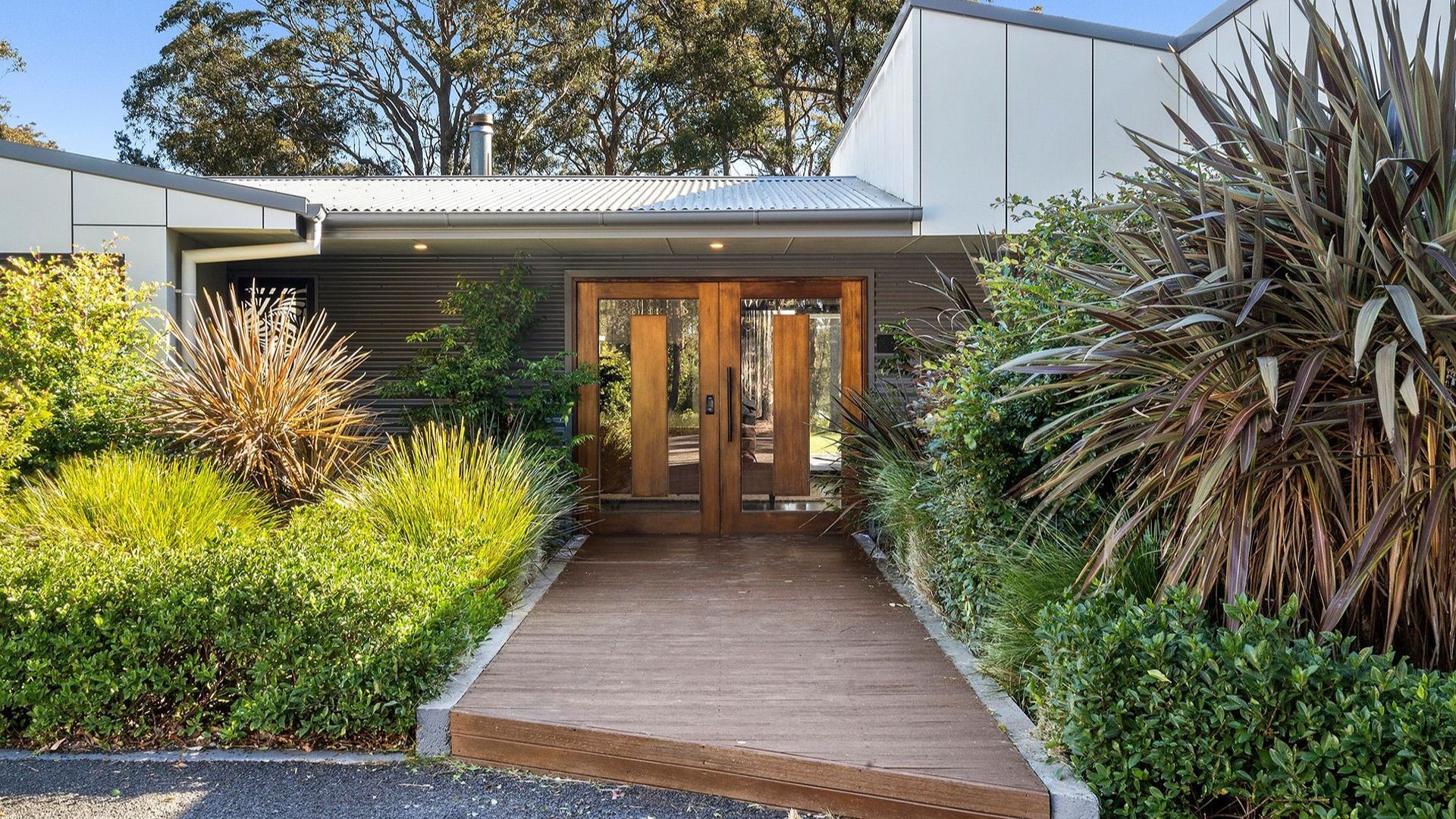 Une maison moderne avec une porte d’entrée en bois, un toit en métal et une allée pavée.