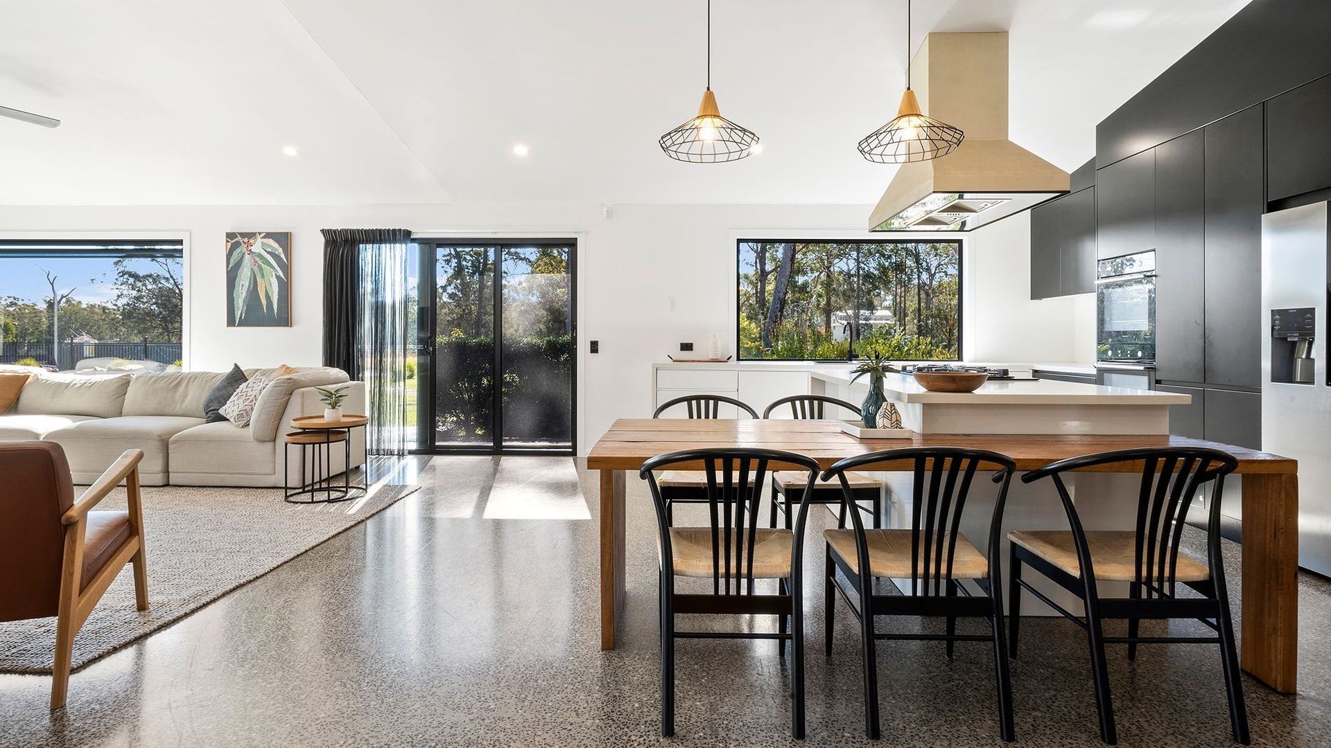 A modern kitchen with a dining area, large windows, and a view of the outdoors.