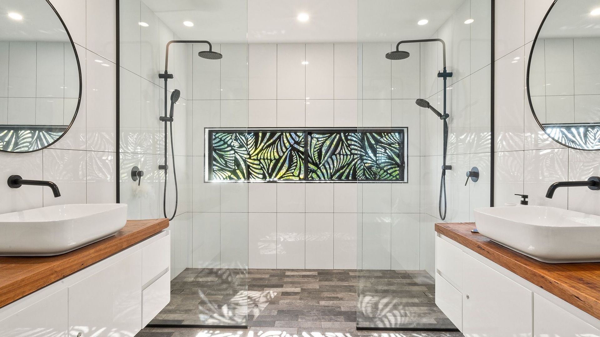 Ein modernes Badezimmer mit zwei Waschbecken, einer Dusche und einem dekorativen Fenster.