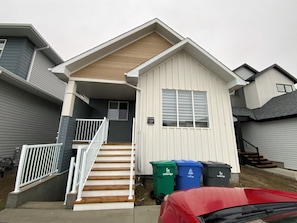 A residential building with a front porch, a staircase, and a garage. - Bright, Spacious & Peaceful | Modern 3BR West Lethbridge Retreat (Lethbridge)