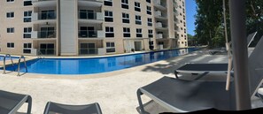 A swimming pool with lounge chairs, a multi-story building with balconies, and a clear sky. - Stay Longer in Jacó - Beach 100m - Pool - Gym (Jacó)