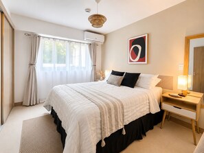 Un dormitorio con cama, mesita de noche, lámpara y ventana con cortinas.