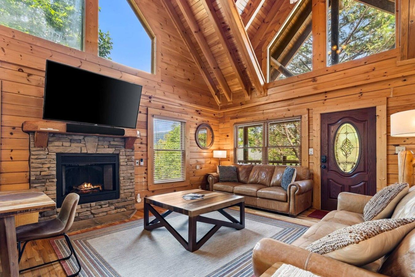 L'intérieur d'une cabane en rondins, avec une cheminée en pierre, un canapé en cuir et un téléviseur à écran plat fixé au-dessus de la cheminée.