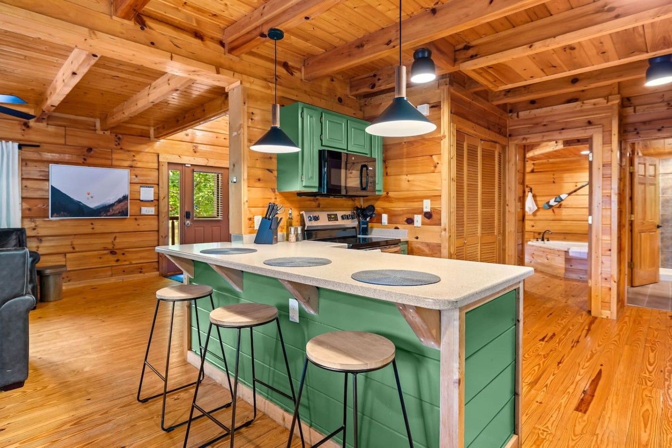 A wooden cabin interior with a kitchen island, bar stools, and a dining area.