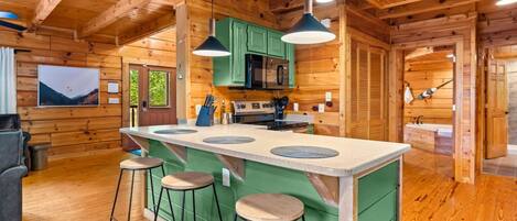 A wooden cabin interior with a kitchen island, bar stools, and a dining area.