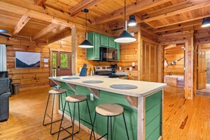 A wooden cabin interior with a kitchen island, bar stools, and a dining area. - Private Creekfront Yard • Karaoke Stage • Fire Pit • Smoky Mountain Lodge (Sevierville)