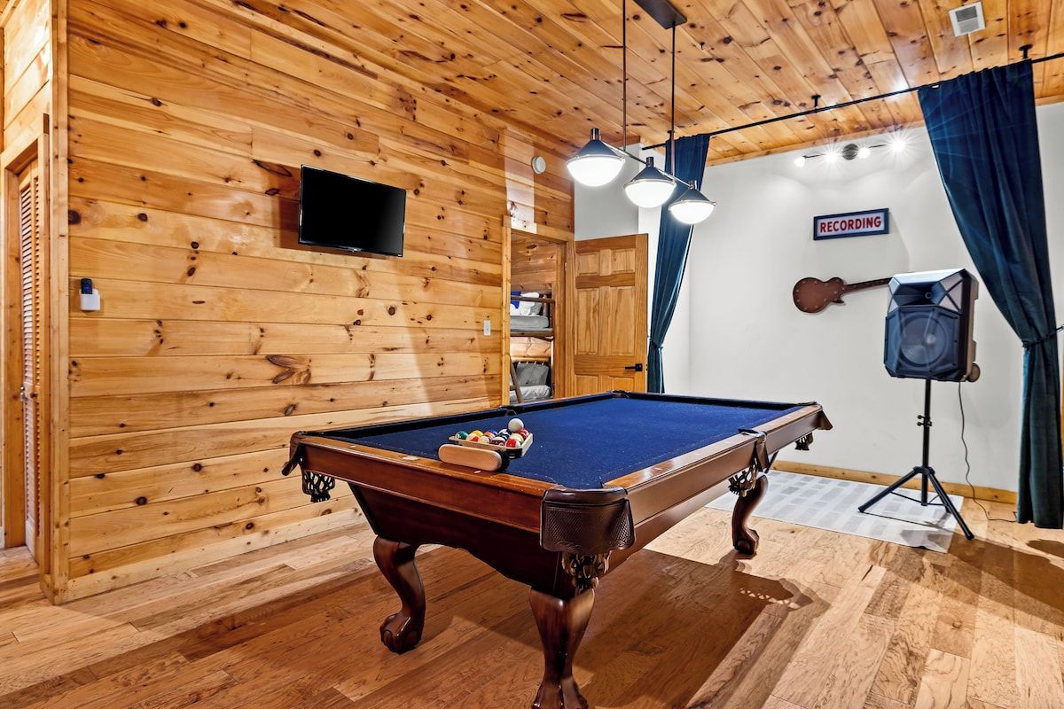 A pool table in a room with wooden walls and a ceiling fan.