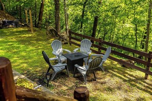 An outdoor seating area with a table and chairs, surrounded by a wooden fence and trees. - Private Creekfront Yard • Karaoke Stage • Fire Pit • Smoky Mountain Lodge (Sevierville)