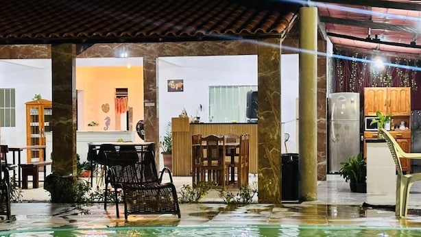 Un espacio al aire libre techado con piscina, mobiliario y una cocina visible al fondo.